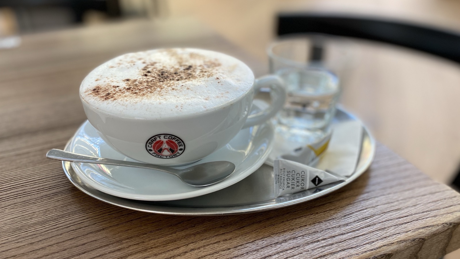 Cappuccino v šálke s logom Craft Coffee Factory na drevenom stole